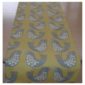 May include: A yellow table runner with a repeating pattern of grey birds. The birds are stylised and have a heart-shaped pattern on their bodies.