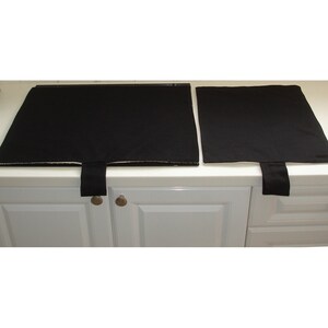 May include: Two black stovetop protectors with fabric edges and a hanging loop. The protectors are on a white countertop.