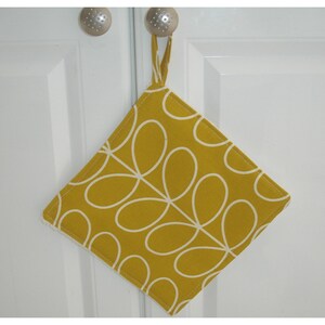 May include: A yellow pot holder with a white stylised leaf pattern. The pot holder has a loop for hanging.
