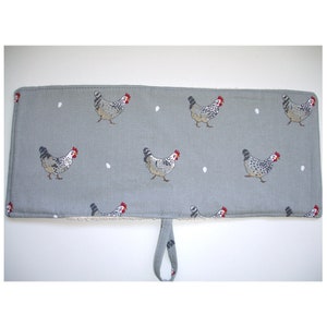 May include: Grey oven mitt with a white and black chicken pattern and white eggs. The mitt has a loop handle.