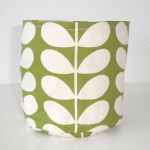 May include: A cylindrical fabric storage basket featuring a repeating pattern of white, rounded leaf shapes arranged in vertical stems against a solid olive green background. The container has a flat base and a simple, open-top design.