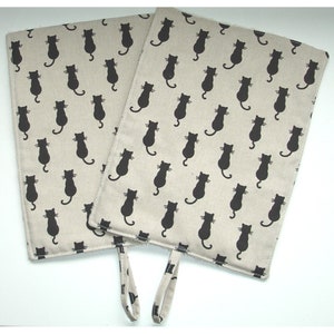 May include: Two beige oven gloves with black cat silhouettes printed all over. The gloves have a loop handle.