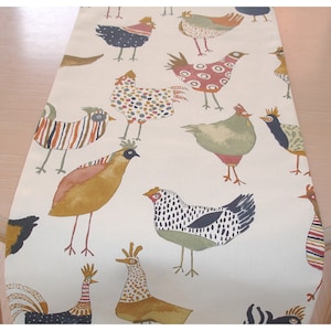 May include: A white table runner with a colorful pattern of chickens. The chickens are illustrated in a whimsical style with various colors, patterns, and poses. The runner is perfect for adding a touch of farmhouse charm to any table setting.