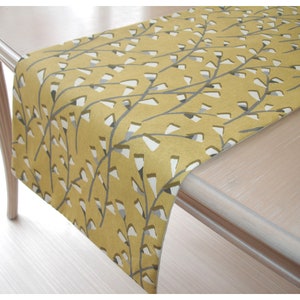 May include: A yellow table runner with a white and gray floral pattern. The runner is made of a soft, woven fabric and has a subtle sheen.