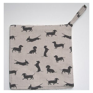 May include: A beige kitchen pot holder with a black dachshund silhouette pattern and a hanging loop.