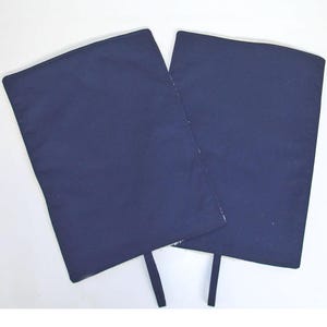 Peut inclure: Deux genouillères en tissu bleu foncé avec des sangles. Les genouillères sont rectangulaires et ont une surface lisse.