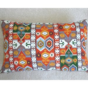 May include: A rectangular pillow with a colorful geometric pattern in shades of red, orange, yellow, blue, green, and white. The pattern is reminiscent of traditional Turkish or Moroccan textiles.