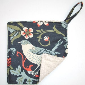 May include: A dark blue pot holder with a floral and bird design. The pot holder is reversible with a soft, beige terry cloth on the back side. It has a loop handle for hanging.