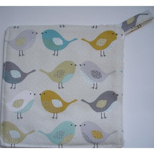 May include: A white cotton pot holder with a hanging loop. The pot holder features a repeating pattern of colourful birds with yellow, blue, grey, and white accents.