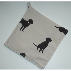 May include: A grey and white pot holder with a black silhouette of a dog repeated on the fabric. The pot holder has a loop for hanging.
