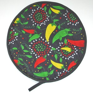 May include: Round black hot pad with a colorful design of red, yellow, and green peppers on a black background. The hot pad has a black fabric handle.