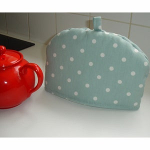Peut inclure: Un chauffe-théière bleu sarcelle à pois blancs. Le chauffe-théière a une anse en boucle sur le dessus.