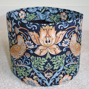 May include: A cylindrical fabric storage basket with a dark blue background and a floral pattern featuring stylized birds, leaves, and flowers in shades of brown, green, white, and orange.