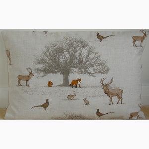 May include: A beige linen cushion cover featuring a woodland scene with a large tree, deer, rabbits, a fox, squirrels, and pheasants. The design is in shades of brown, orange, and grey.