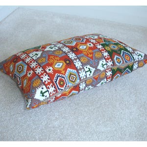 May include: A long rectangular pillow with a colorful geometric pattern in shades of red, orange, yellow, blue, green, and white. The pillow has a zipper closure.