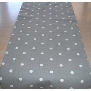 May include: A grey table runner with white polka dots. The runner is made from a soft, cotton fabric and is ideal for adding a touch of elegance to any table setting.