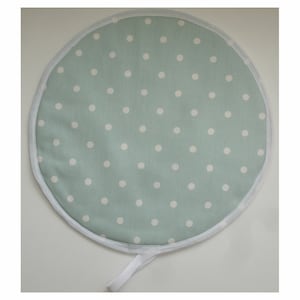 May include: A round, light blue pot holder with a white polka dot pattern and a white trim. It has a white loop handle.