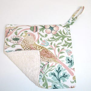 May include: A white cotton dishcloth with a floral pattern featuring a pink and brown bird. The dishcloth has a cream-coloured terry cloth backing and a loop for hanging.