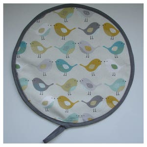 May include: Round grey and white pot holder with a pattern of colourful birds. The birds are yellow, blue, grey, and white.