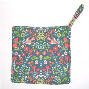 May include: A square, teal pot holder with a floral and bird pattern. The design features red flowers, green leaves, and stylized birds. A matching fabric loop is attached for hanging. The pot holder is likely made of cotton.
