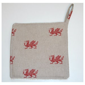 May include: A beige linen pot holder with a red Welsh dragon design. The pot holder has a loop for hanging.