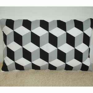 May include: A rectangular pillow with a geometric pattern of black, white, and gray cubes. The pillow is made of fabric and has a soft, plush texture.