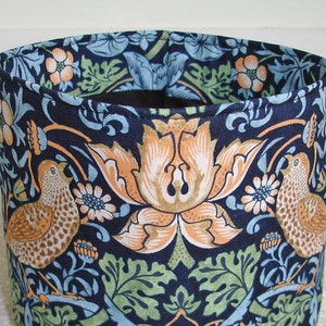 May include: A blue and brown fabric storage basket with a floral pattern featuring birds and stylized flowers. The basket is made of a sturdy fabric and has a round shape.