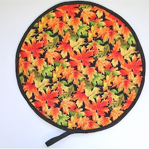 May include: Round black and white hot pad with a design of orange, yellow, and green maple leaves. The hot pad has a black fabric handle.
