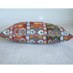 May include: A long rectangular pillow with a colorful geometric pattern in shades of red, orange, yellow, blue, green, and brown. The pillow has a zipper closure.
