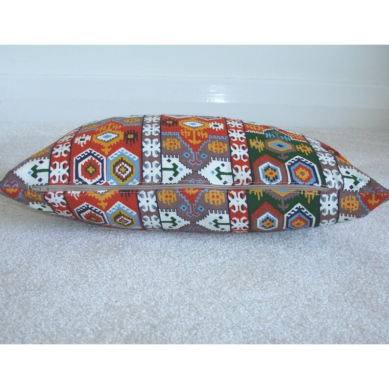 May include: A long rectangular pillow with a colorful geometric pattern in shades of red, orange, yellow, blue, green, and brown. The pillow has a zipper closure.