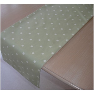 May include: A green table runner with white polka dots. The runner is lying on a wooden table.