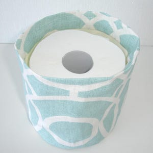 May include: A cylindrical fabric storage basket featuring a light mint green and white geometric pattern. The basket contains a single roll of white toilet paper, which is visible from the top opening of the container.