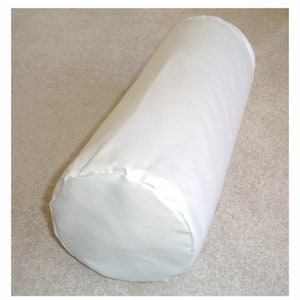 May include: White cylindrical pillow with a smooth fabric cover. The pillow is lying on a light beige carpet.