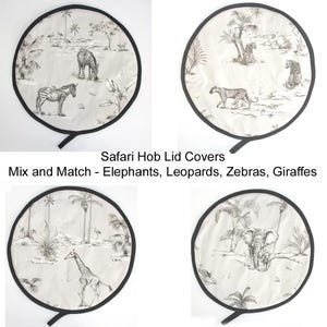 May include: Four circular hob lid covers with black edging, each displaying a different black and white safari scene. The illustrations include zebras, leopards, giraffes, and elephants. The text reads "Safari Hob Lid Covers" and "Mix and Match - Elephants, Leopards, Zebras, Giraffes".