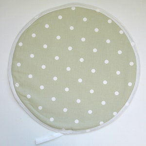 May include: A circular, pale green cushion featuring a white polka dot design. It has a white trim and a white fabric loop. This cushion is suitable for home decor, with a diameter of approximately 30 cm.