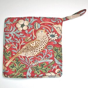 May include: Square red oven glove with a bird and floral pattern. The glove features a repeating design of a bird, flowers, and leaves in shades of brown, green, and blue. A loop is attached for hanging.