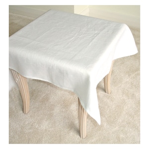 May include: A white linen tablecloth draped over a light wood table with turned legs.