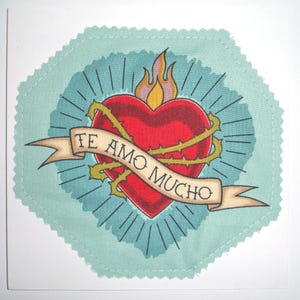 May include: A teal blue fabric heart with a red heart inside, surrounded by thorns and a banner that reads "Te Amo Mucho".