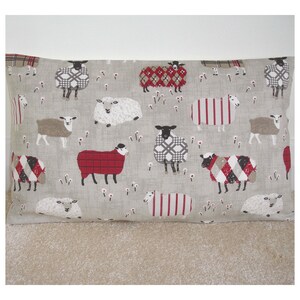 May include: A beige cushion cover with a repeating pattern of sheep in various colors and designs. The sheep are wearing red, white, and black plaid patterns.