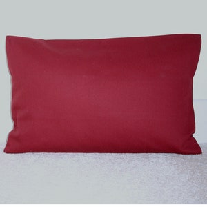 May include: A solid red rectangular cushion with a smooth, even surface. The cushion is lying flat on a white, fluffy surface.