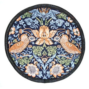 May include: Circular navy blue fabric trivet with a black trim. The design features a symmetrical pattern of orange, blue, and green flowers and birds. Two birds face each other, surrounded by stylized floral elements.