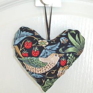 May include: A heart-shaped fabric ornament with a black background and a colorful floral pattern. The ornament features a bird with a brown, green, and blue pattern, and red strawberries.
