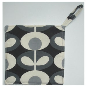 May include: A black and white pot holder with a geometric pattern of circles and stems. The pot holder has a loop handle.