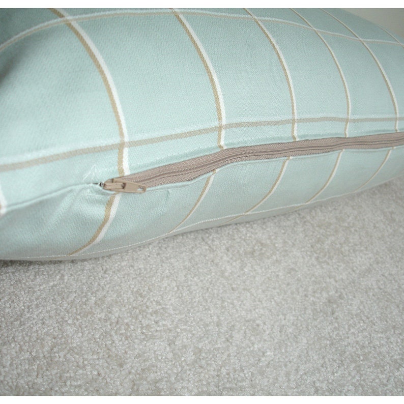 May include: A light blue pillow with a tan and white plaid pattern. The pillow has a zipper closure.