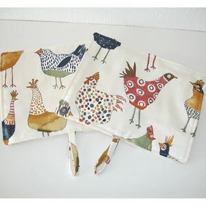 May include: Off-white fabric featuring colourful, quirky chicken illustrations. The chickens are decorated with patterns like polka dots and stripes. The fabric is likely intended for use in kitchen textiles or home decor items.