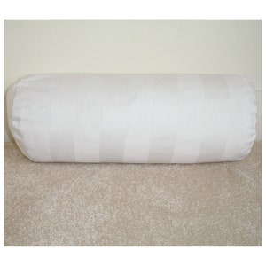 May include: White cylindrical pillow with horizontal stripes. The pillow is on a light brown carpet.