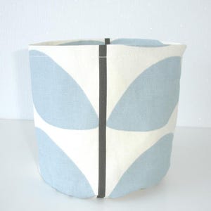May include: A cylindrical fabric storage basket featuring a repeating pattern of light blue petal shapes on an off-white background, accented by a single vertical dark gray seam running down the center of the exterior surface.