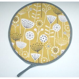 May include: Round yellow pot holder with a grey trim and a grey handle. The pot holder has a pattern of white and grey stylised flowers on a yellow background.
