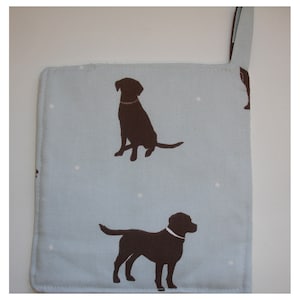 May include: A light blue pot holder with a white polka dot pattern and two brown silhouette images of Labrador Retrievers.