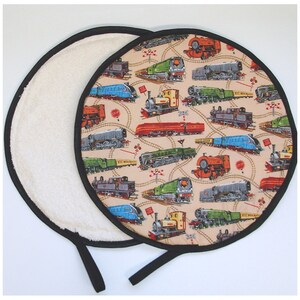 May include: Round, reversible pot holder with a black trim. One side is white terry cloth. The other side features a colorful print of vintage train engines on a beige background.